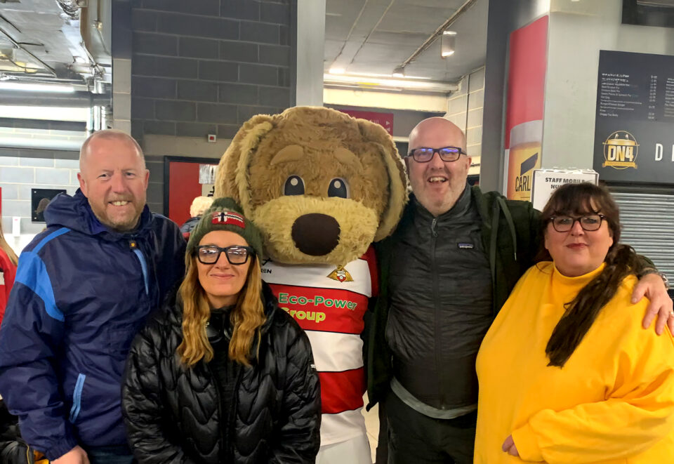 Four people smiling next to dog football mascot